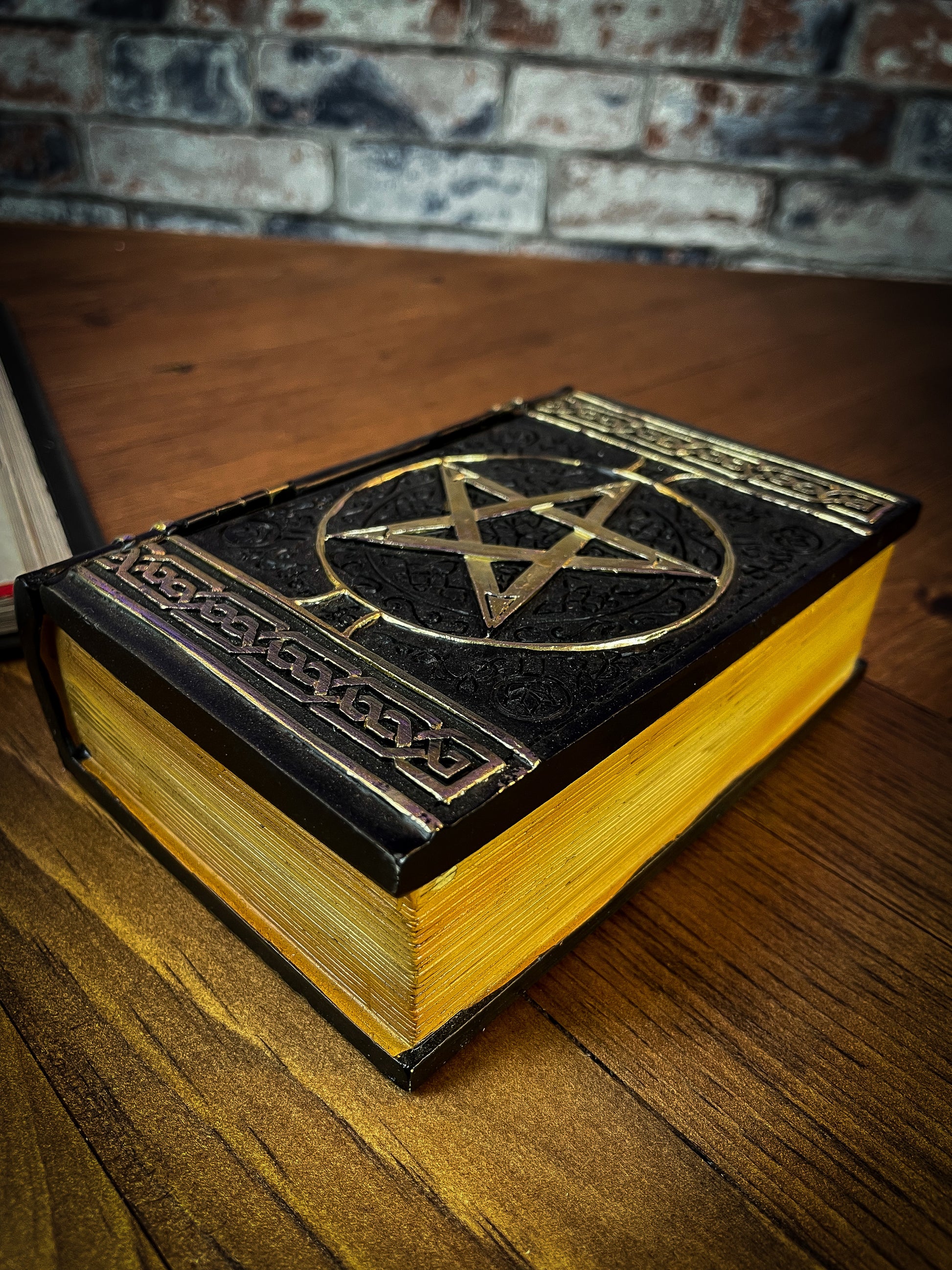 This fantastic box can subtly blend into any arcane library. Taking form of an ancient book, bound in black leather. The lid of the box features a raised golden pentagram with detailed patterns decorating the top and bottom of the cover. Free UK Delivery with Fandomonium
