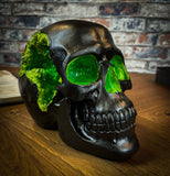 The most unassuming facade can hide the most scintillating interior. This matte black skull has eyes and nose holes that open up to a sparkling green world. A large crack at the side of the skull reveals an enchanting green crystal geode within, sparkling in the light. Free UK Delivery by Fandomonium